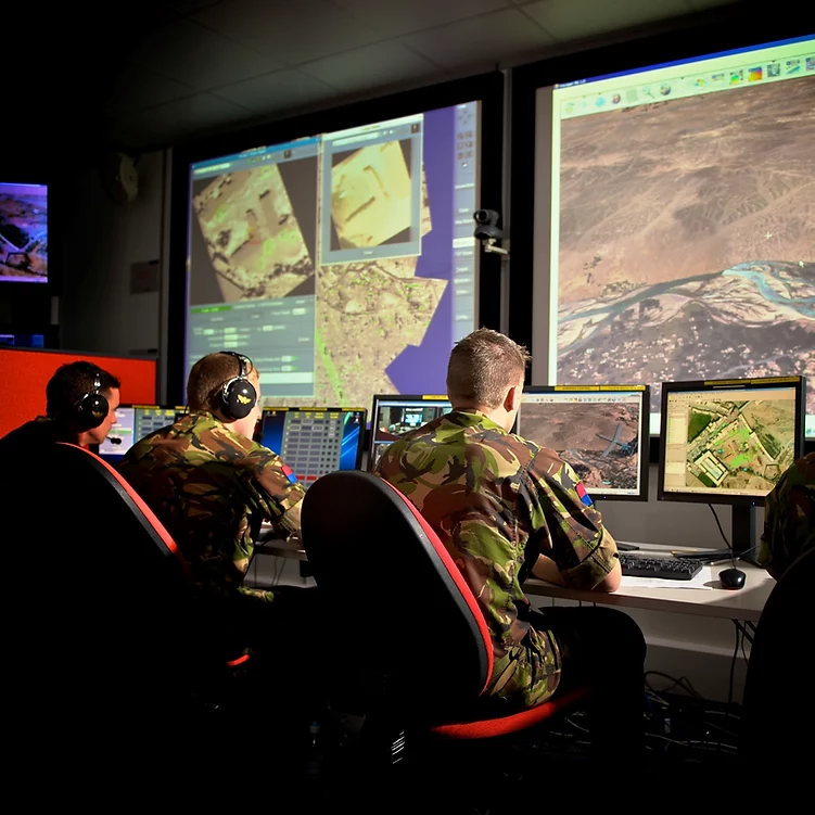 Soldiers looking at screens that display a skyview of the battlefield.